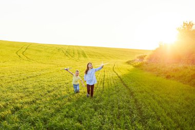 Koşan çocuk ve kız ellerinde iki sarı ve mavi uçak oyuncağı yaz güneşli bir günde tarlada