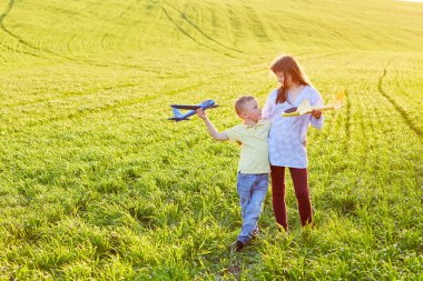 Koşan çocuk ve kız ellerinde iki sarı ve mavi uçak oyuncağı yaz güneşli bir günde tarlada