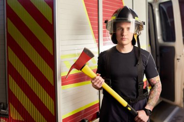 İtfaiyeci kasklı ve baltayla itfaiye arabasının karşısında.. 