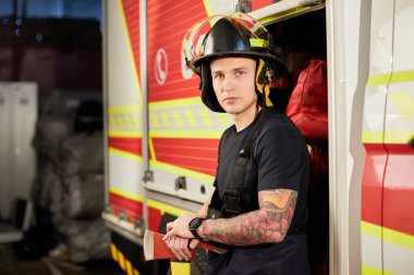 İtfaiyeci kasklı ve baltayla itfaiye arabasının karşısında.. 