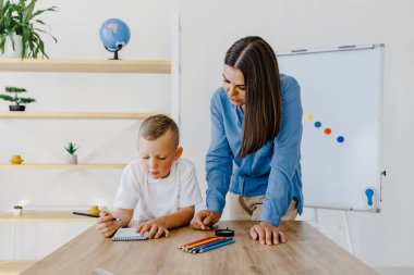 Private lesson. Attentive young woman tutor teacher helping little boy pupil with studying, correct mistakes explain learning material. Smiling mother assist small boy with home task