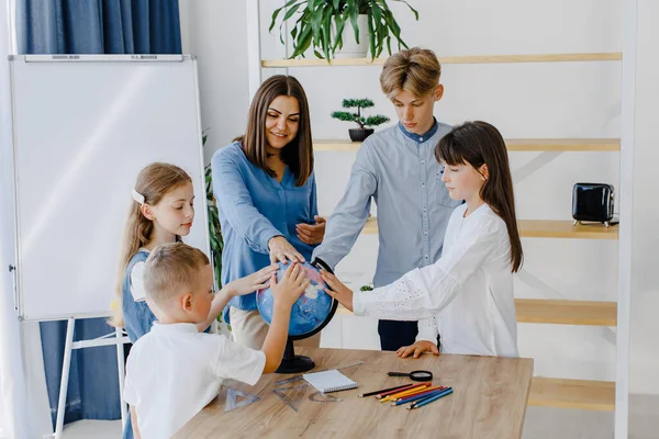 Dünya 'ya dokunuyor. Farklı yaşlarda bir grup çocuk okuldaki geniş bir sınıfta duruyorlar ve öğretmenler dünyaya dokunuyor..