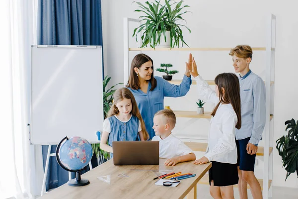 Mutlu orta okul öğrencileri, matematik dersinde birlikte çalışarak online yazılım öğrenme web eğitim teknolojisini kullanarak dizüstü bilgisayarlara bakarak öğretmenler masasında toplandı...