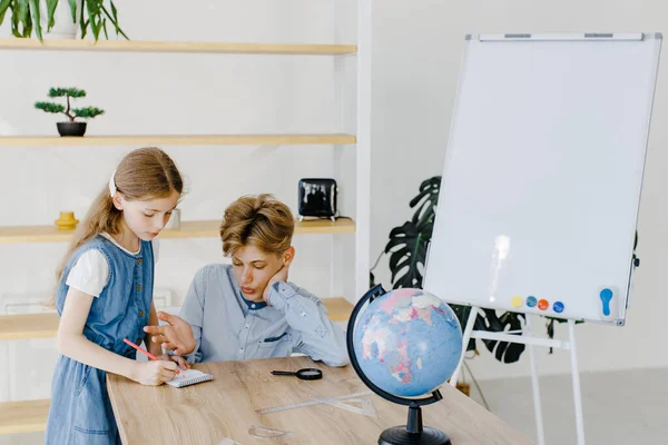 Genç bir kız ve oğlan, sınıflarında dünya ile birlikte masanın yanında oturuyorlar. Okul çocuğu ve liseli kız okulda birlikte proje yapıyorlar.