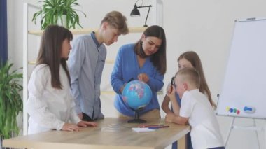 Sınıftaki çocuklar ve öğretmenler küreye bakıyor, öğretmen sınıftaki çocuklara masadaki dersi açıklamaya yardım ediyor. Eğitim okulu süreci, parlak oda ve ilginç öğrenme