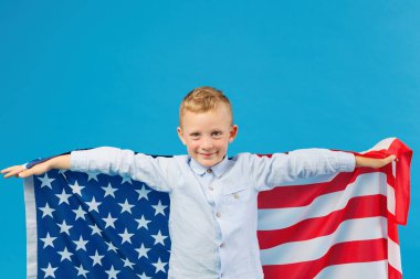 Stüdyoda mavi arka planda Amerikan bayrağı tutan sevimli çocuk. Ülkeye karşı vatanseverlik kavramı