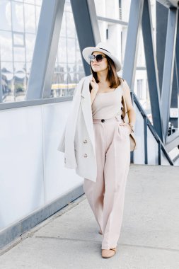 Beautiful brunette businesswoman wearing suit and white hat, walking on the street. Beautiful woman walking to the meeting