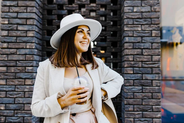 Beautiful woman going to meeting with cold coffee walking on the street. Portrait of successful business woman holding cup of cold drink in hand on her way to work on city street