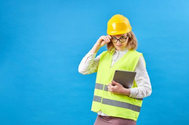 Tabletle çalışan iş kadını müteahhiti. Stüdyoda gülümseyen kadın mavi arka planda. İnşaat, onarım, dekorasyon konsepti