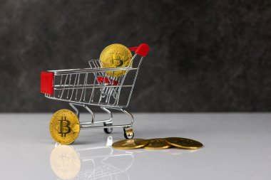 Bitcoin in shopping trolley on dark grey background in white table. Future currency concept.