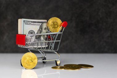 Bitcoin and roll of dollars in shopping cart or basket on dark grey background. Buy or Sell. The concept of the impact of virtual currency on the economy.