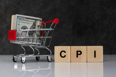 Roll of dollars in shopping cart and wooden blocks with the word cpi on dark grey background. Buy or Sell. Business and CPI, consumer price index concept