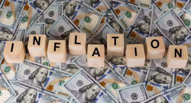 Wooden cubes with text inflation on US dollar money banknotes. The idea for FED considers interest rate hikes, world economics, and inflation control. Concept shows rising inflation. The impact of the war on the world economy.