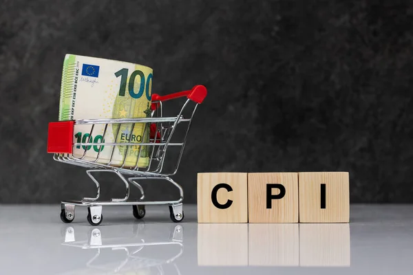 Cash money rolls in shopping trolley, euro banknotes whith wooden blocks with word CPI on white table on dark grey background. CPI, consumer price index symbol