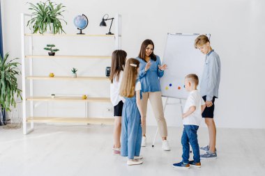 Explaining lesson and using board. Group of children students of different ages in class at school with teacher.