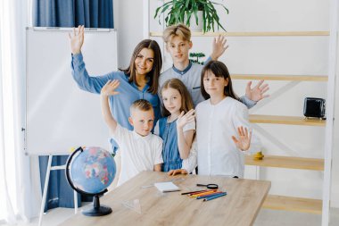 Farklı yaşlarda bir öğretmen ve okul çocukları geniş bir sınıfta kameraya bakarak gülümsüyor. Öğrenme kavramı