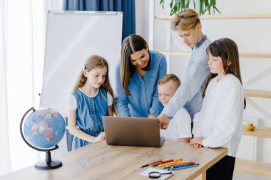 Mutlu orta okul öğrencileri, matematik dersinde birlikte çalışarak online yazılım öğrenme web eğitim teknolojisini kullanarak dizüstü bilgisayarlara bakarak öğretmenler masasında toplandı...