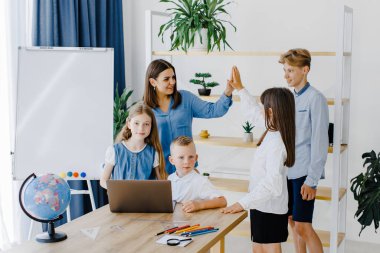 Mutlu orta okul öğrencileri, matematik dersinde birlikte çalışarak online yazılım öğrenme web eğitim teknolojisini kullanarak dizüstü bilgisayarlara bakarak öğretmenler masasında toplandı...