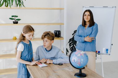 Two students are working on a project at school in a spacious classroom. The teacher observes the students' learning process