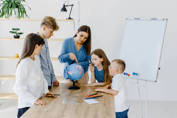 Sınıftaki çocuklar ve öğretmenler küreye bakıyor, öğretmen sınıftaki çocuklara masadaki dersi açıklamaya yardım ediyor. Eğitim okulu süreci, parlak oda ve ilginç öğrenme