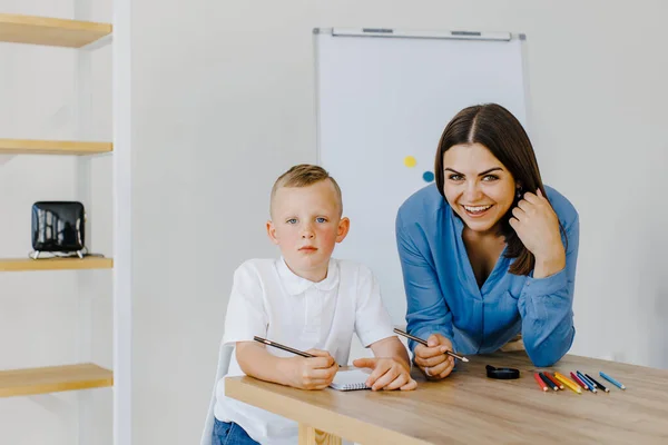 Private lesson. Attentive young woman tutor teacher helping little boy pupil with studying, correct mistakes explain learning material. Smiling mother assist small boy with home task