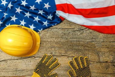 Yellow helmet and gloves with American flag on old wooden table, space for text. Labor day
