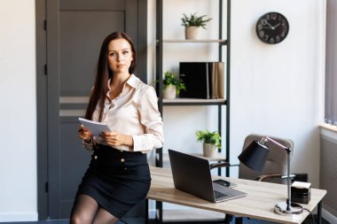 Happy business woman using pen and writing something in her notebook, raising her hand up, showing a greeting gesture