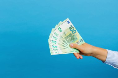 Woman's hand holding hundred euros banknotes isolated on blue background. Euro money, cash banknotes