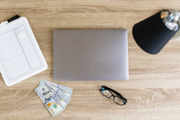 Top view of desktop with weekly planner, laptop, glasses, lamp and cash dollar bills. The concept of planning expenses for the week