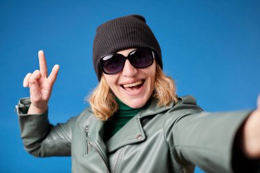 Pretty caucasian woman taking selfie, looking at camera POV and showing two fingers gesture, point of view of photo.