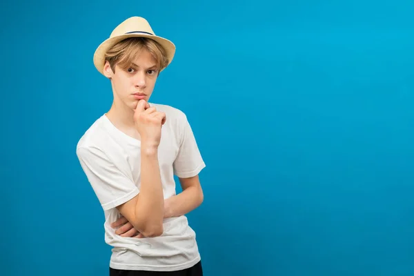 Let me think. Young caucasian boy wearing casual white t-shirt serious face thinking about question with hand on chin, thoughtful about confusing idea
