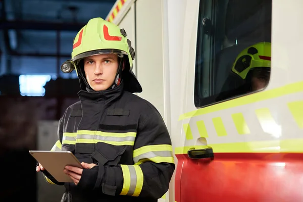 Male firefighter with tablet in uniform on car background