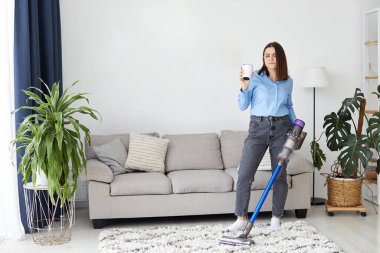 Elektrikli süpürgeyle kahve içen kadın.