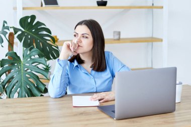 Konsantre iş kadını evdeki masada dizüstü bilgisayarla otururken evrak hazırlıyor.