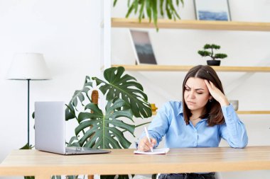 Konsantre iş kadını evdeki masada dizüstü bilgisayarla otururken evrak hazırlıyor.