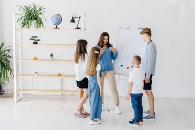 Explaining lesson and using board. Group of children students of different ages in class at school with teacher.
