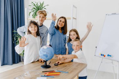 Sınıftaki çocuklar ve öğretmenler küreye bakıyor, öğretmen sınıftaki çocuklara masadaki dersi açıklamaya yardım ediyor. Eğitim okulu süreci, parlak oda ve ilginç öğrenme