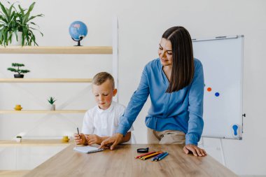 Private lesson. Attentive young woman tutor teacher helping little boy pupil with studying, correct mistakes explain learning material. Smiling mother assist small boy with home task