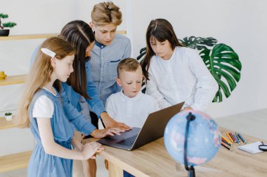 Mutlu orta okul öğrencileri, matematik dersinde birlikte çalışarak online yazılım öğrenme web eğitim teknolojisini kullanarak dizüstü bilgisayarlara bakarak öğretmenler masasında toplandı...