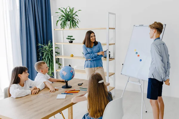 A teacher and students of different ages at a geography lesson. The student answers by standing near the board and tells the story