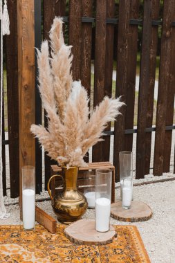 Vazodaki yüksek otlar ve dekorasyon partisindeki ahşap çitlere karşı cam ampullerde mumlar. Pampas otları iç kısımda, boho tarzı. Düğün için dekor.