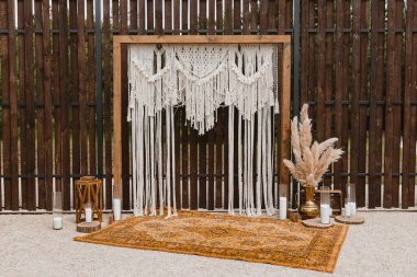 Beautiful bohemian type arch decoration on outdoor wedding ceremony venue on backyard. Florist flower compositions with pampas grass near carpet, string fairy lights. Summer rural wedding.
