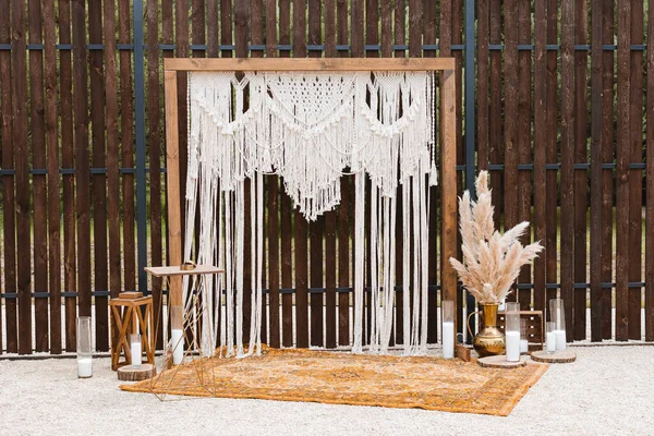 Beautiful bohemian type arch decoration on outdoor wedding ceremony venue on backyard. Florist flower compositions with pampas grass near carpet, string fairy lights. Summer rural wedding.