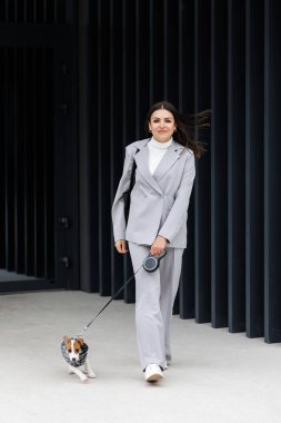 En sevdiği tüylü, eğitimli Jack Russell Terrier köpeğiyle gezen sıradan bir kadın sonbahar günü açık havada, duvarın yanında köpekler için takım elbise giymiş. Sadık en iyi arkadaşlar