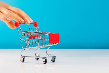 İş ve e-ticaret kavramı. Stüdyoda mavi bir arka planda dururken boş bir alışveriş arabasını iten parmakları kullanarak yakın plan. Yan görüş. Metin için boşluk