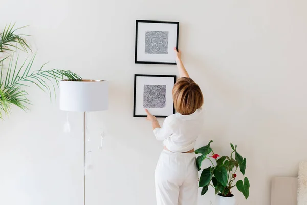 Woman hanging pictures on wall in room. Interior design