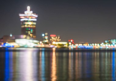 Defocused skyline of Amsterdam at night, blurred lights of traffic and modern buildings around IJ river nearby central station