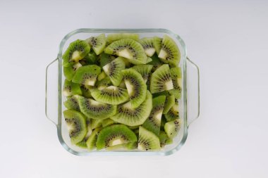 Beyaz arkaplanı olan cam kare bir kabın içindeki kivi meyve dilimleri veya kesme parçaları.