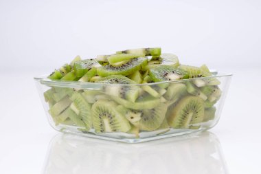 Beyaz arkaplanı olan cam kare bir kabın içindeki kivi meyve dilimleri veya kesme parçaları.