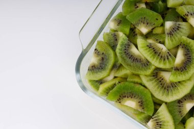 Beyaz arkaplanı olan cam kare bir kabın içindeki kivi meyve dilimleri veya kesme parçaları.